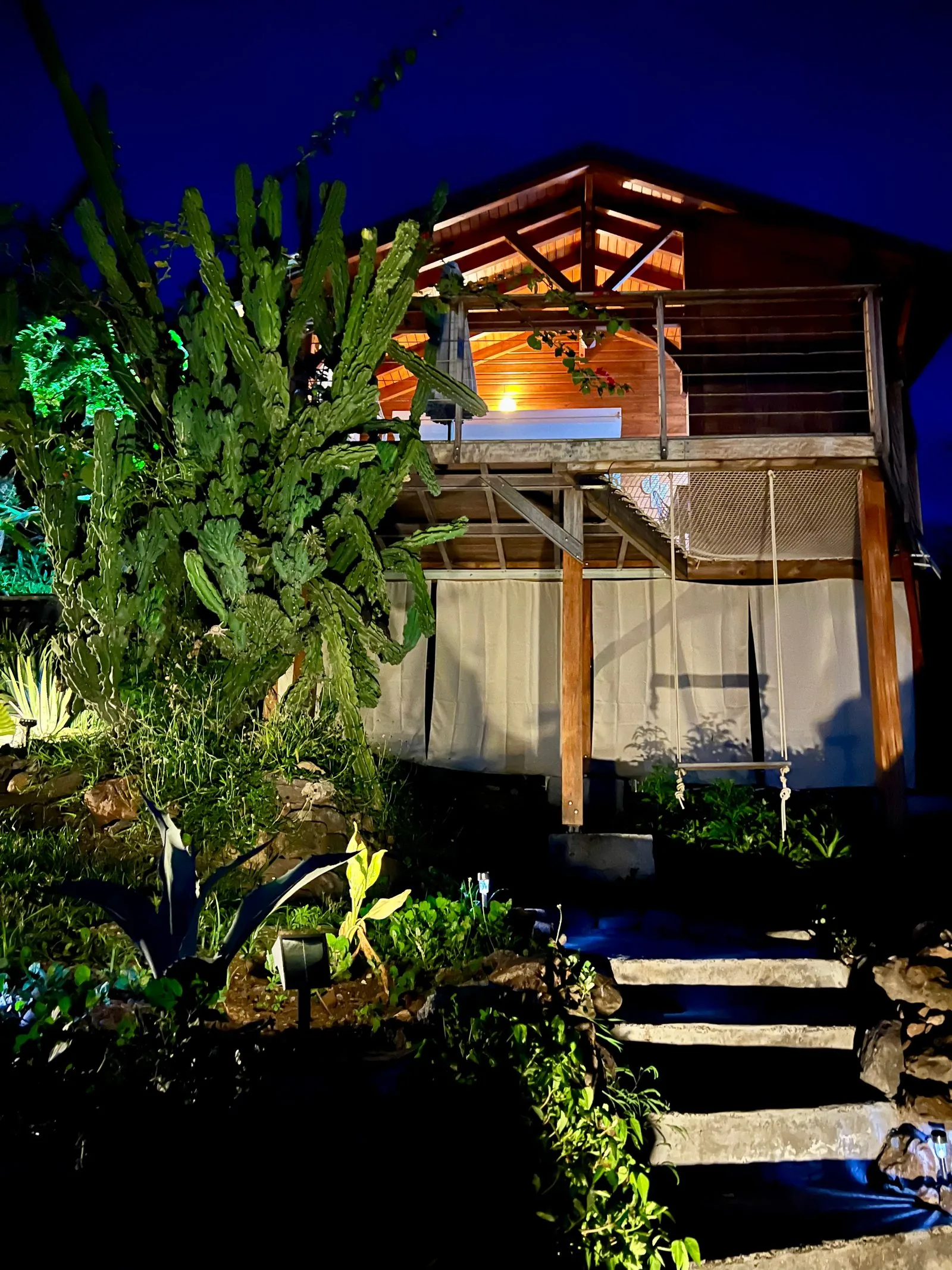 Façade du bungalow sur pilotis illuminée la nuit, entourée de végétation tropicale